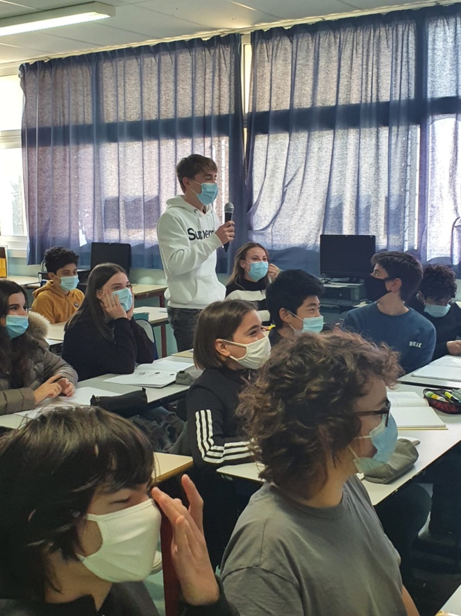 Photo de la classe avec un élève debout tenant un micro et parlant